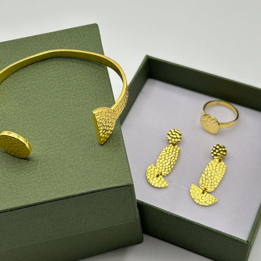 Vergoldeter Armreif, Ring und Ohrrhinge auf beigem Hintergrund, Schmuckset